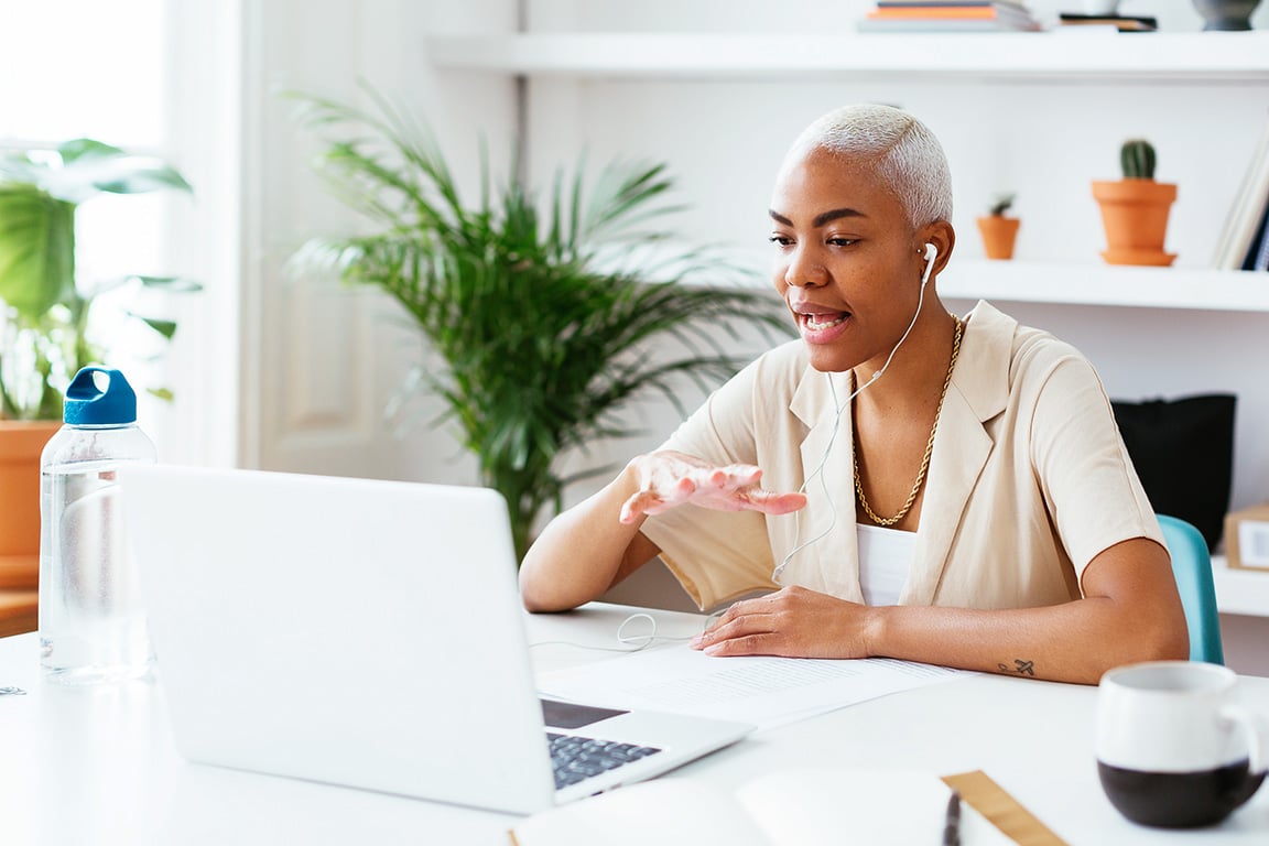 person with earbuds sits in front of laptop for video conference