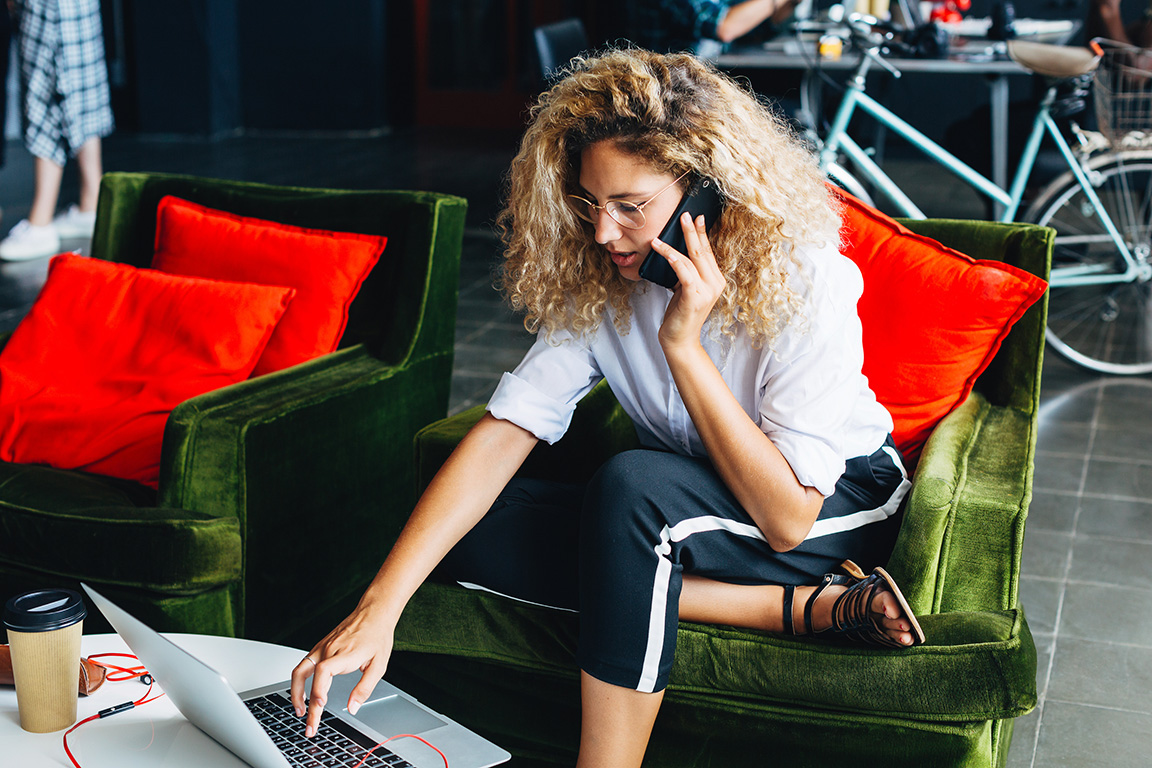 A woman working on her laptop while talking on the phone. 