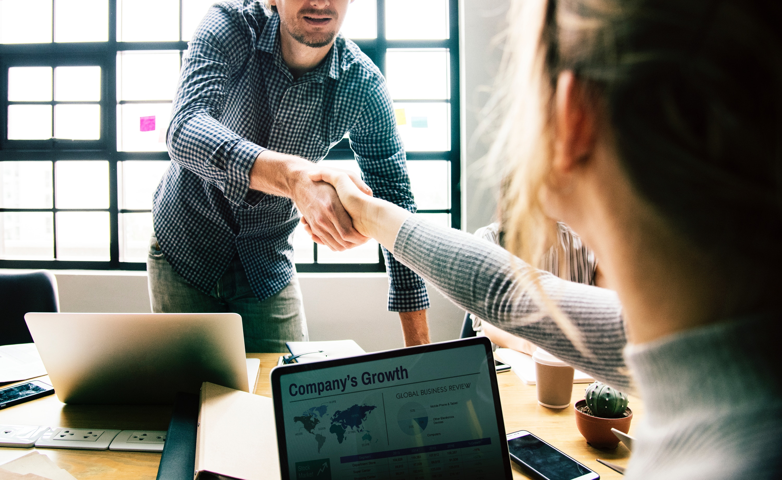 Two colleagues on laptops shaking hands over the meeting table
